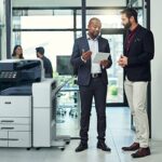 Deux hommes dans un bureau discutent sur une tablette à côté d'une imprimante multifonction couleur Xerox® AltaLink® série C8200 Deux hommes dans un bureau discutent sur une tablette à côté d'une imprimante multifonction couleur Xerox® AltaLink® série C8200
