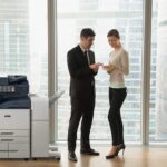 Deux personnes en tenue professionnelle dans un bureau discutent de documents à côté d'une imprimante multifonction Xerox® AltaLink® série B8200 Deux personnes en tenue professionnelle dans un bureau discutent de documents à côté d'une imprimante multifonction Xerox® AltaLink® série B8200